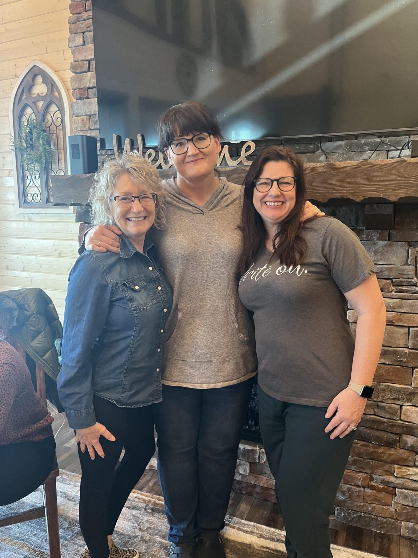 Three women standing next to each other in front of a fireplace.