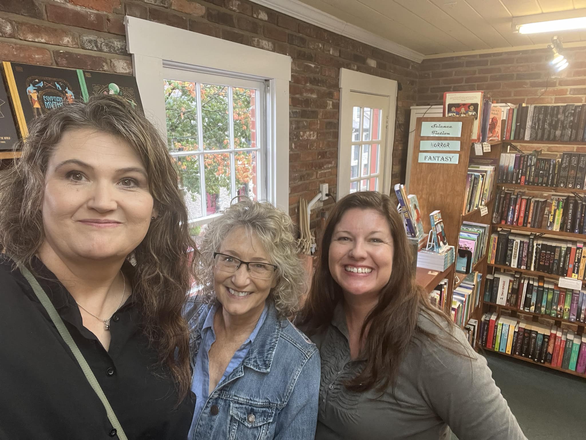 Three women standing in a room with books on the wall.